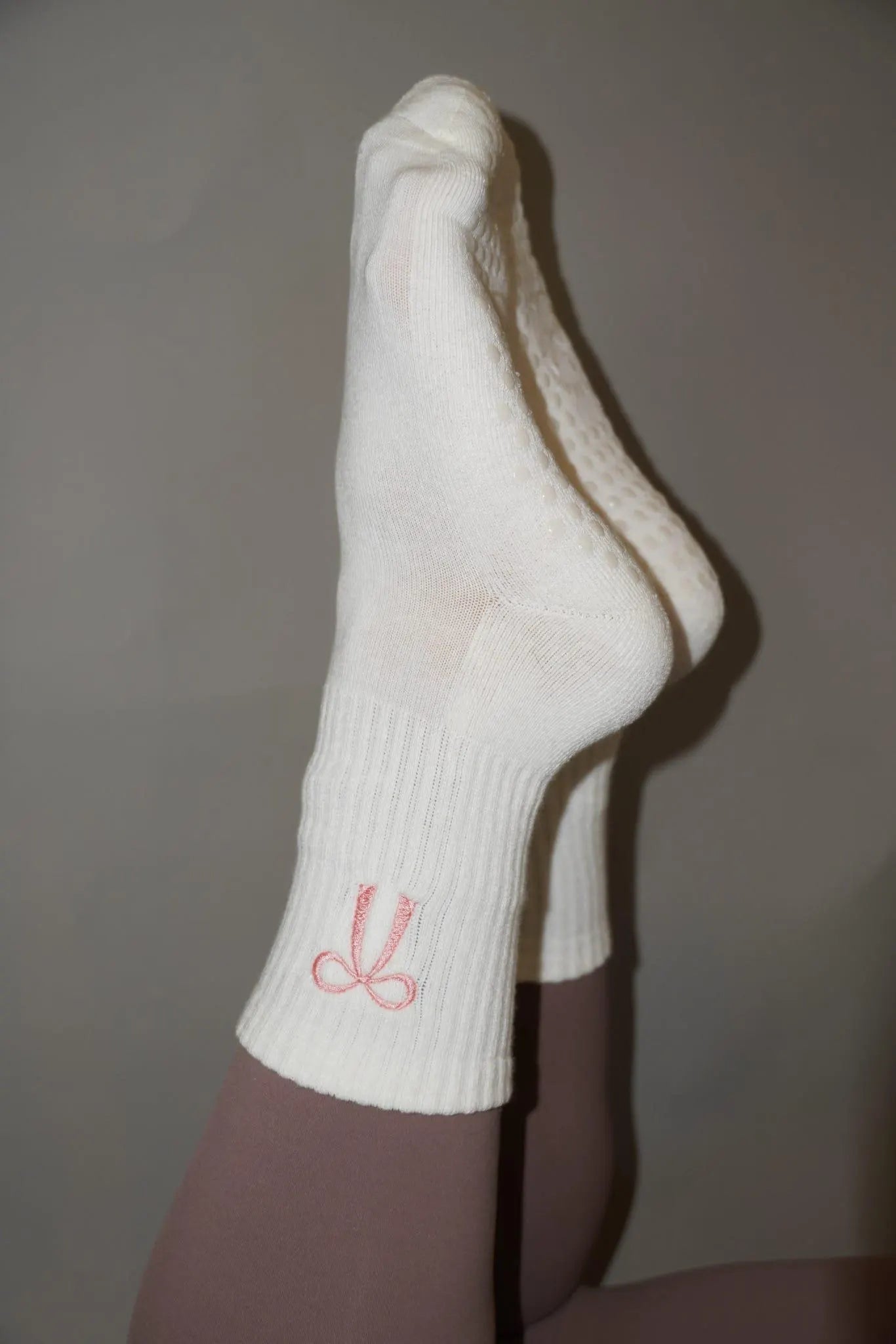 white grip socks on a persons feet with a pink coquette bow embroidered on them
