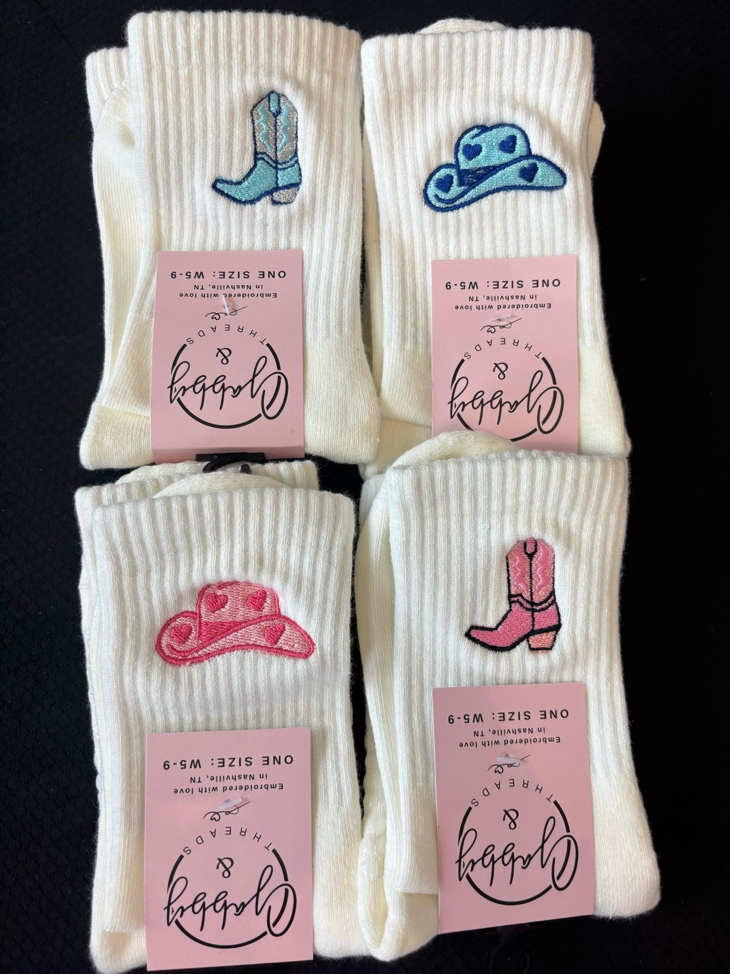Four pairs of white socks with embroidered cowboy hats and boots on a black background