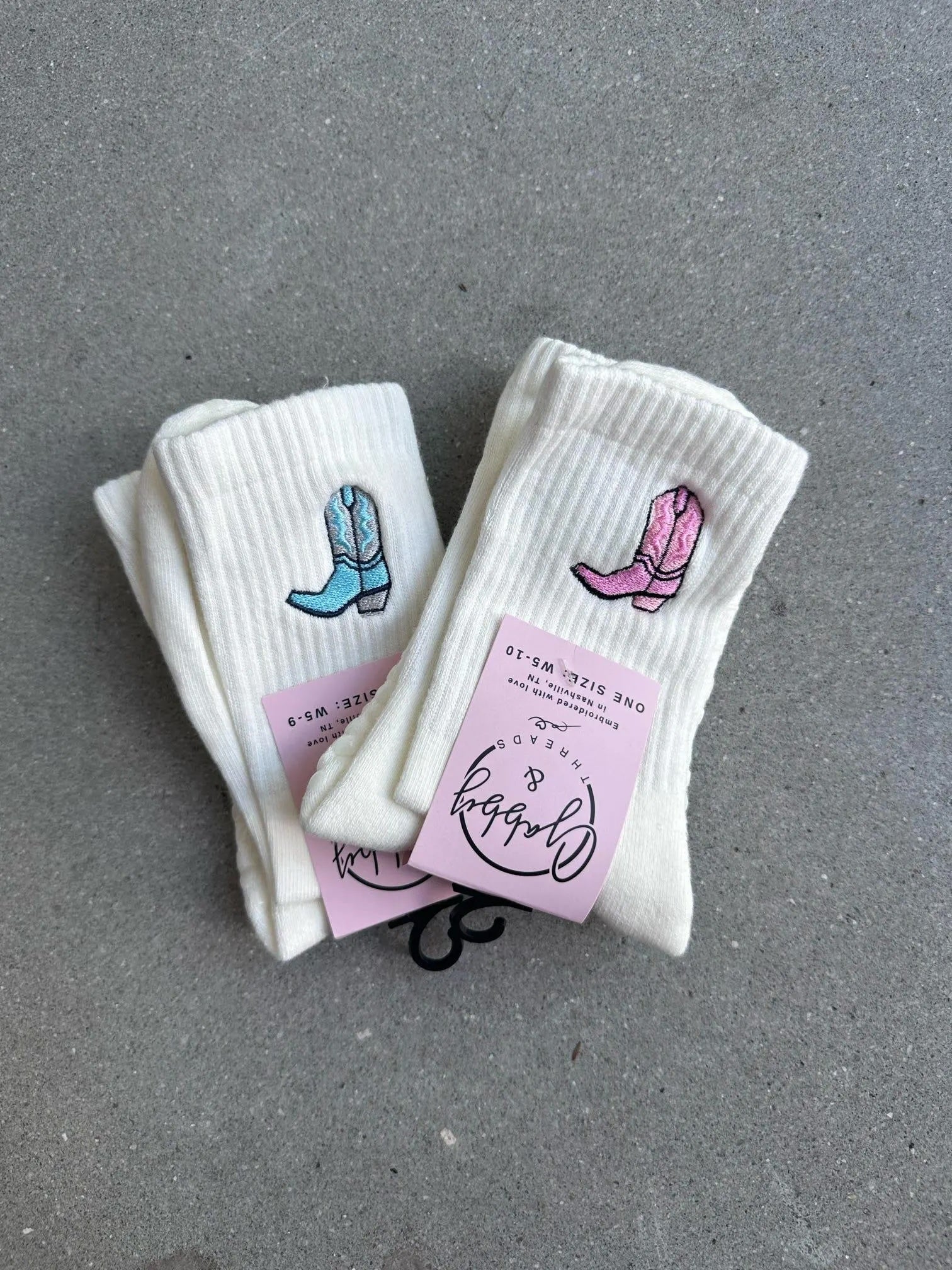 two pairs of white grip socks with an embroidered cowboy boot against a grey background