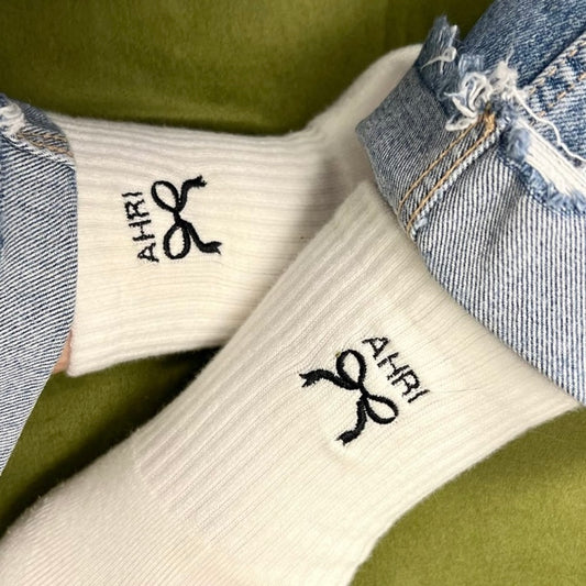 White socks with black coquette bow and the name 'AHRI' on a green background