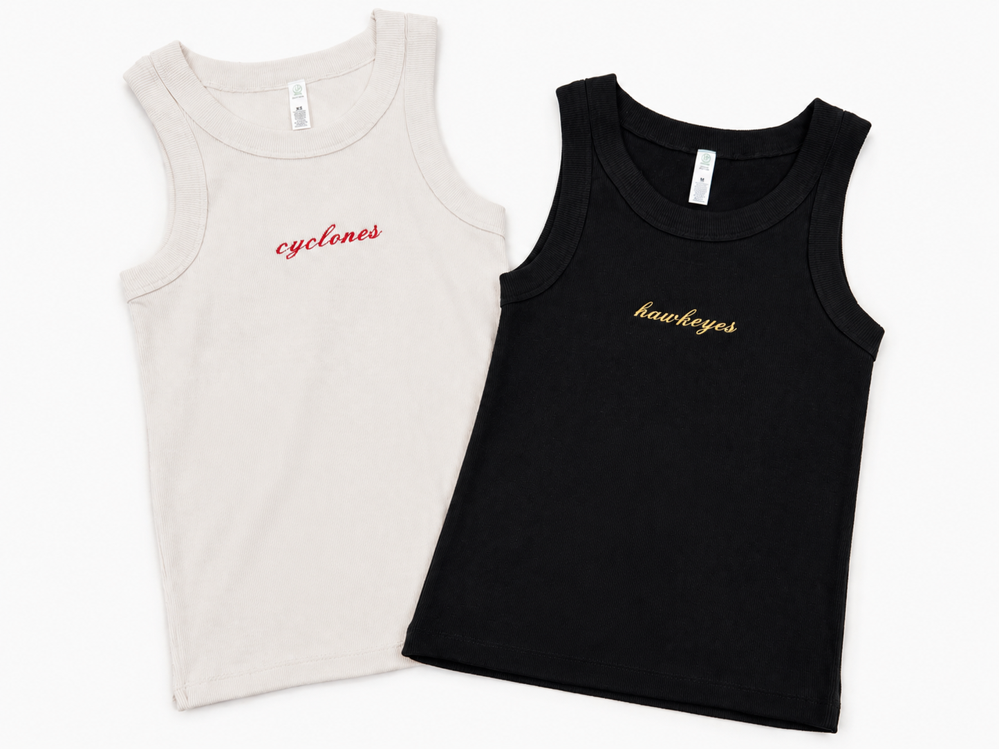 Two sleeveless tank tops laid flat on a white background: one off-white with red script text reading 'cyclones' and one black with gold script text reading 'hawkeyes'.