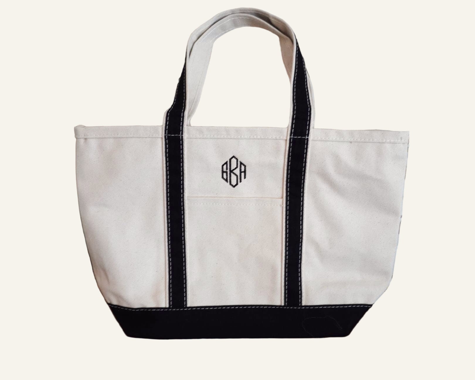 White tote bag with black trim monogrammed with 'GBA'.