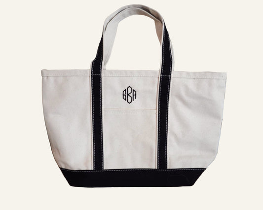 White tote bag with black trim monogrammed with 'GBA'.