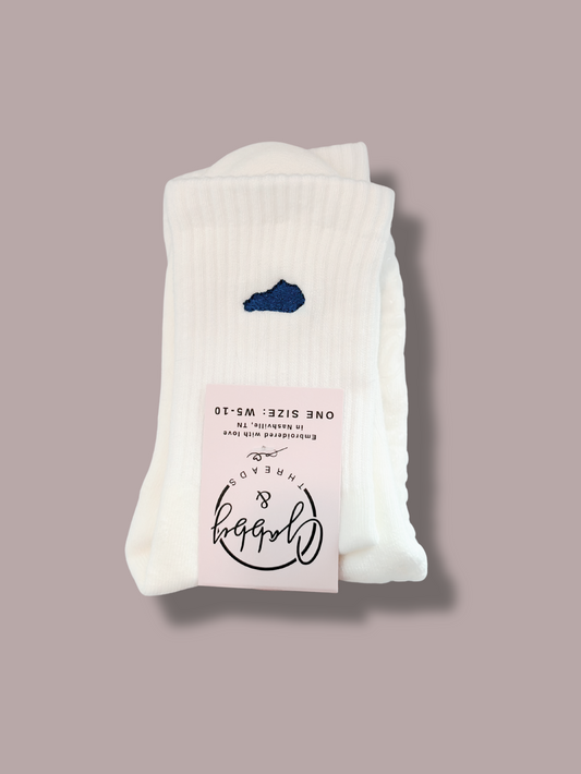White everyday crew socks with state of Kentucky embroidered on it in blue thread against a purple background