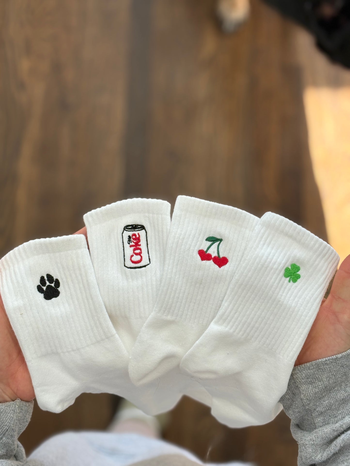 4 white crew socks with different icons: black paw print, diet coke, cherry heart, green clover