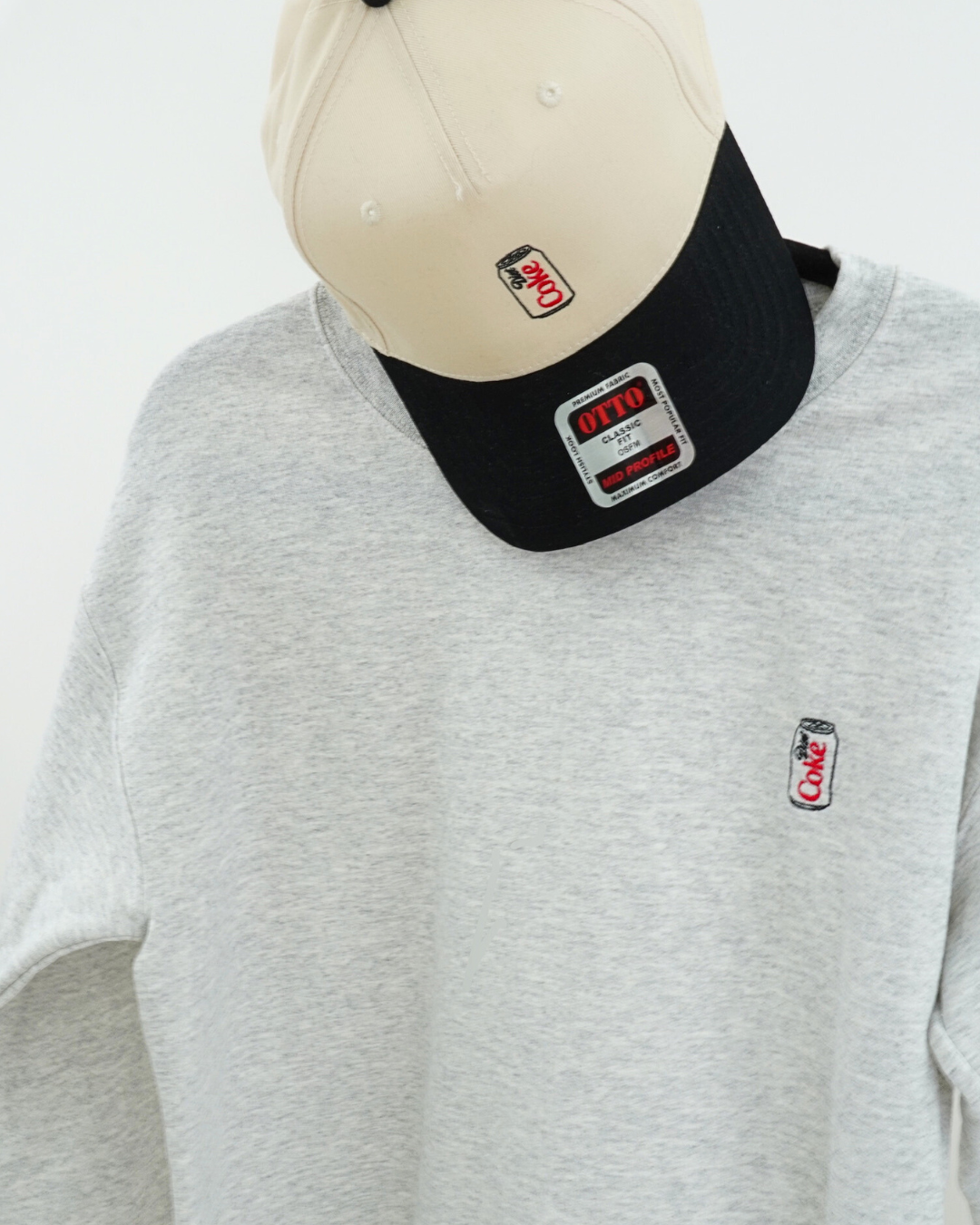 Gray sweatshirt with black cap featuring a logo on a white background