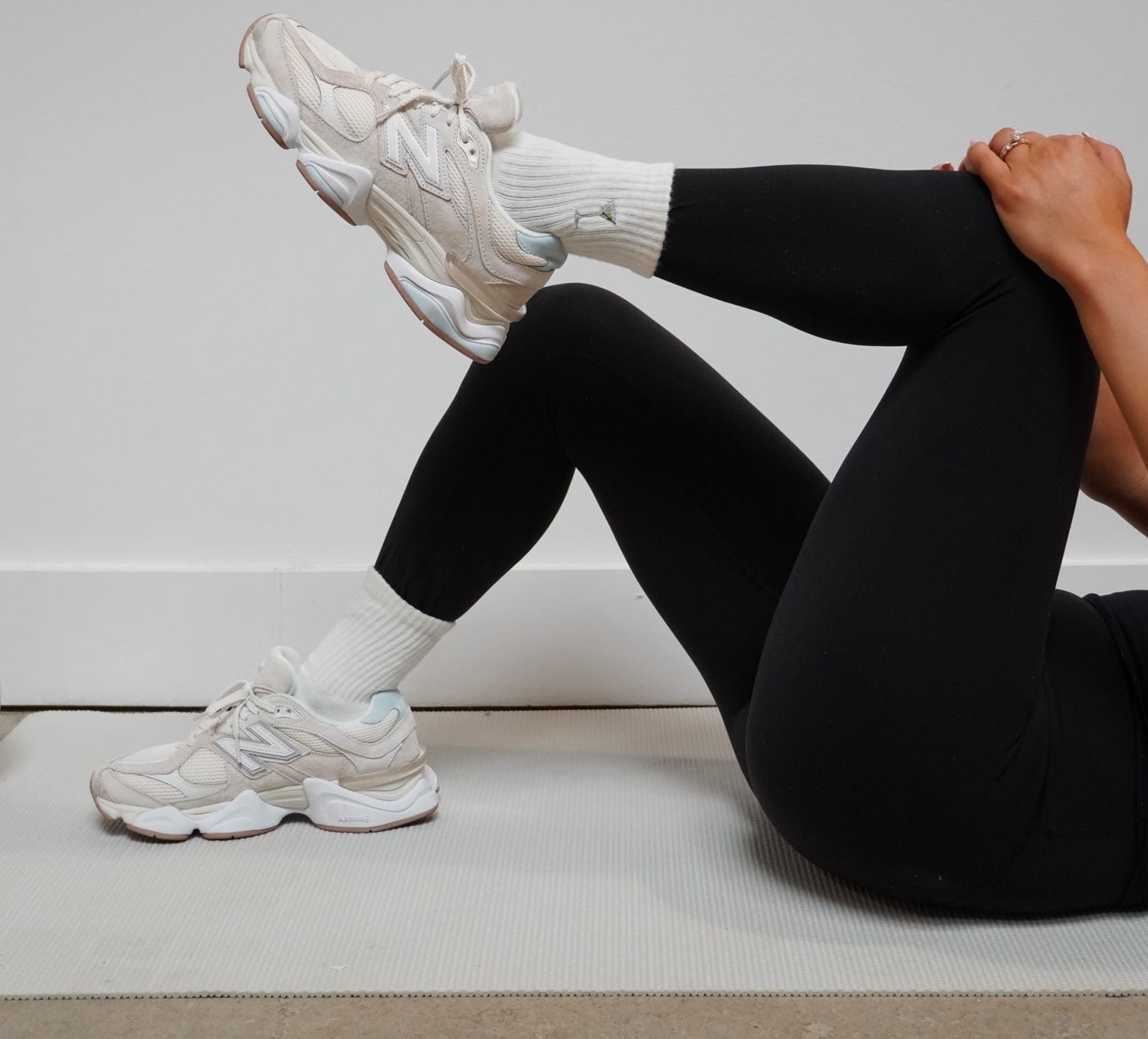 Person wearing black leggings and white sneakers sitting on a yoga mat with dirty martini socks on