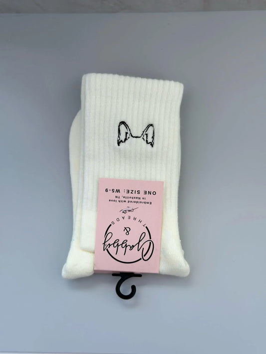 a pair of white grip socks with embroidered dog ears on them lay against a grey background