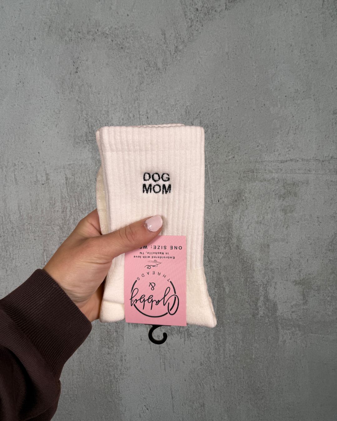 A pair of white socks with the text "dog mom" embroidered on them against a grey background