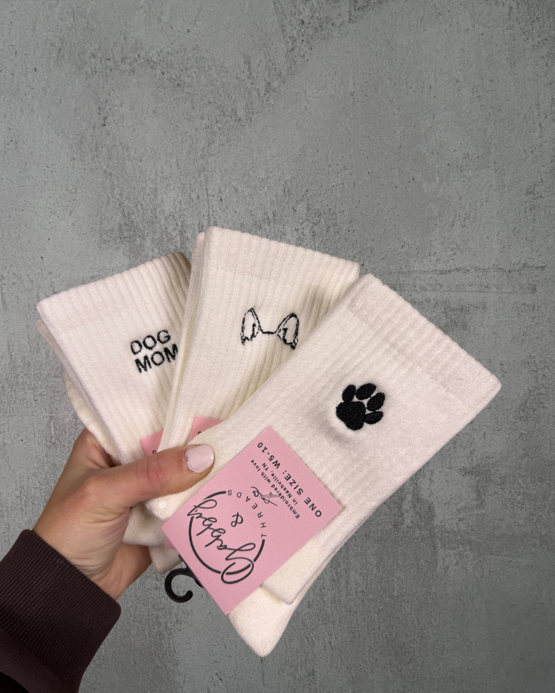 Set of white socks with dog-themed designs held by a hand against a gray background