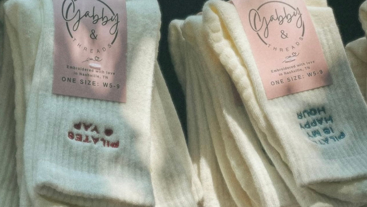 White embroidered socks with personalized text on a black background, featuring 'Gabby & Threads' brand labels
