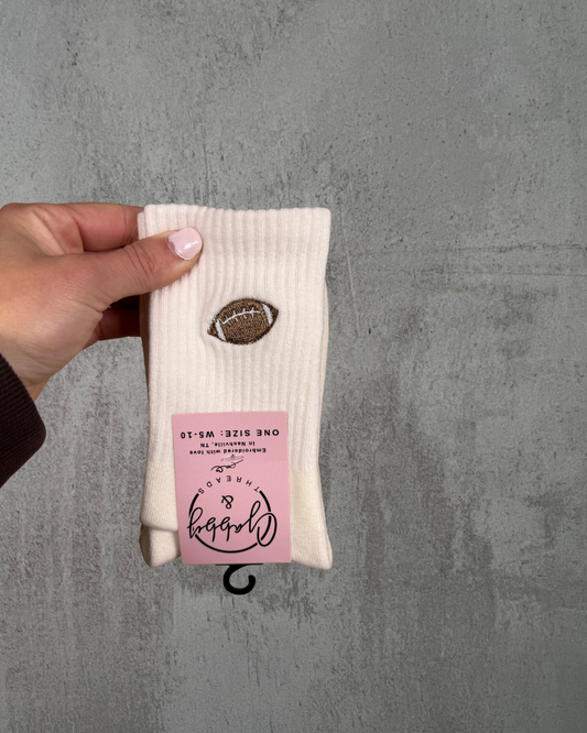 a hand holds up a pair of white crew socks with an embroidered football on them