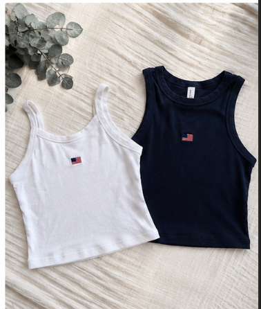 Two tank tops, one white and one black, on a textured surface with eucalyptus leaves.