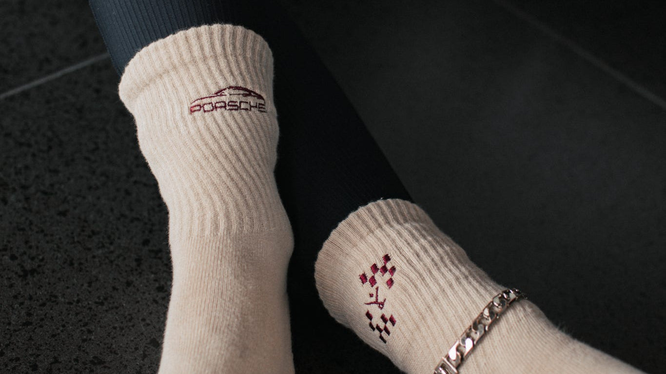 Beige socks with Porsche logo worn on a dark surface.