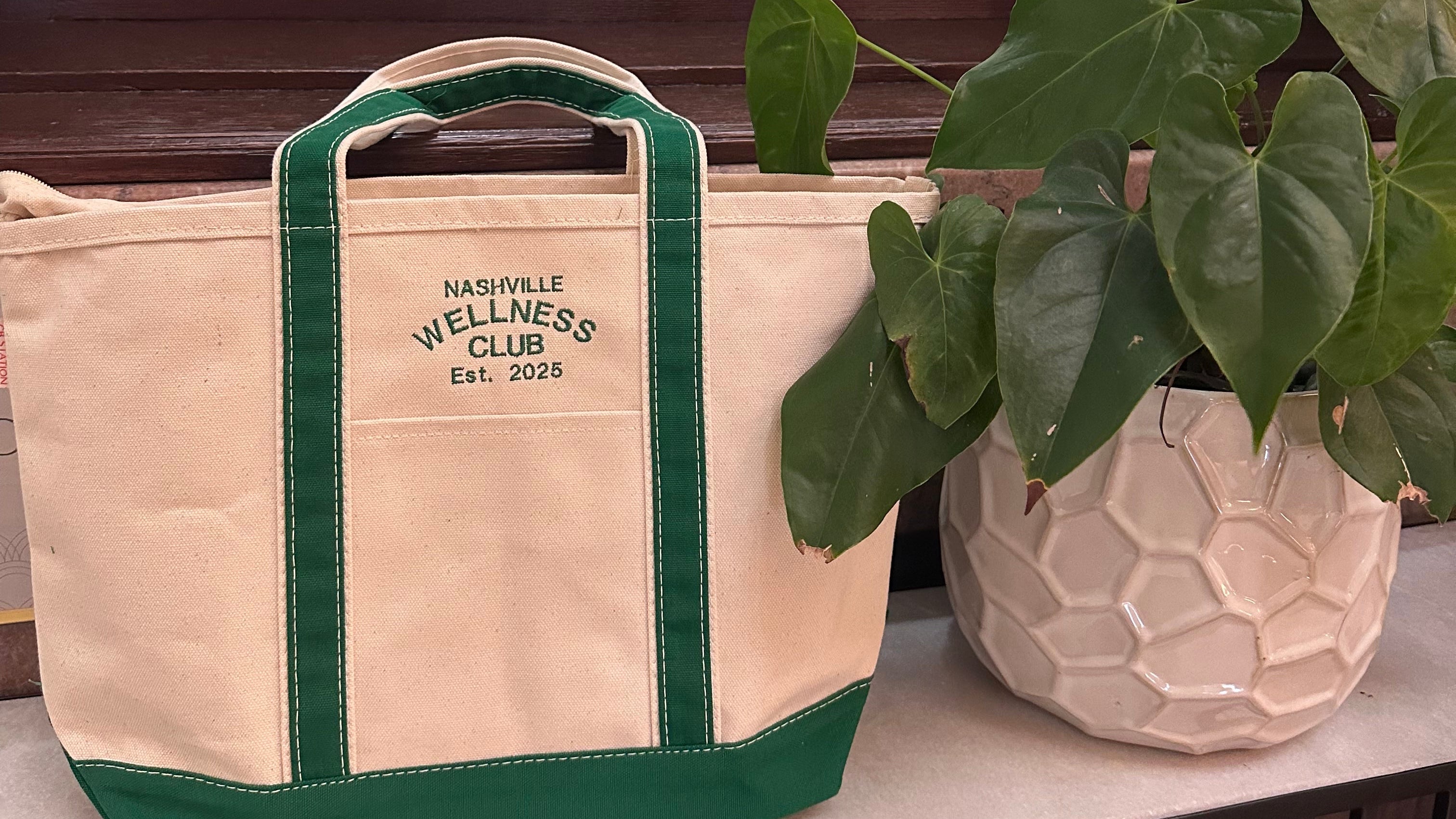 Customized beige tote bag with green accents on a windowsill next to a plant.