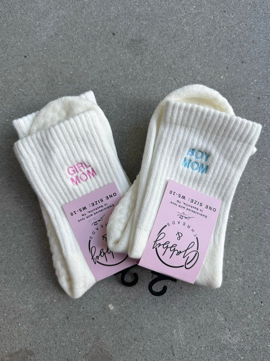 White socks with 'Girl Mom' and 'Boy Mom' text on labels against a gray background