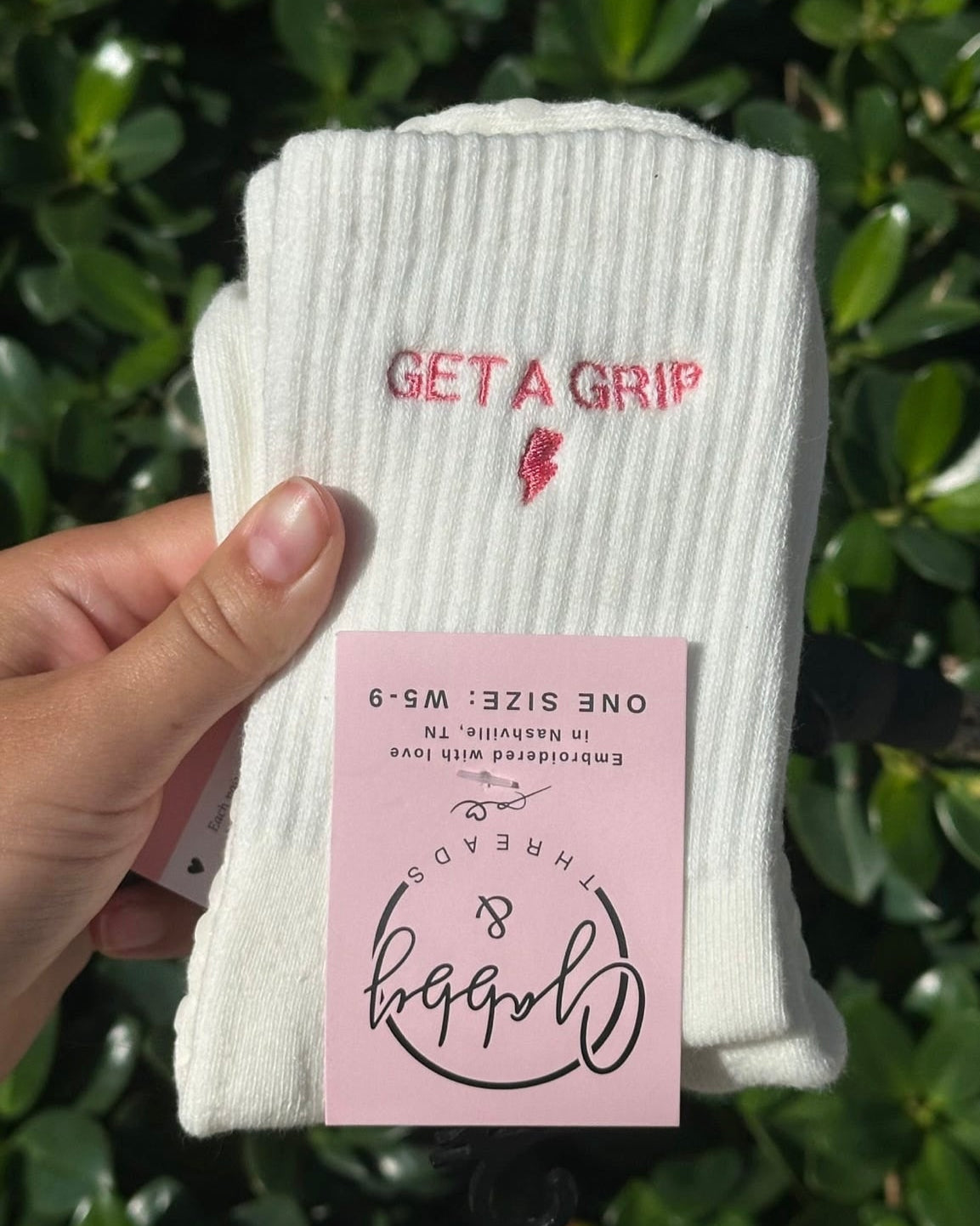 White socks with 'GET A GRIP' text held by a hand against a green leafy background
