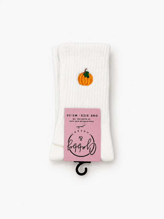 a pair of white socks against a white background with an orange Halloween Pumpkin embroidered on it 