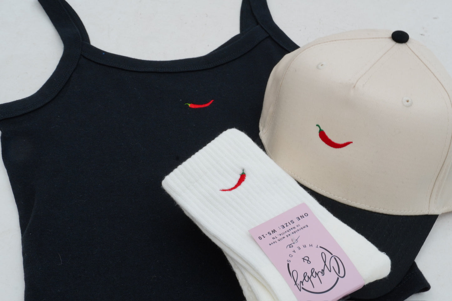 a black embroidered tank with a red pepper, a hat with a red pepper and a pair of socks with a red pepper embroidered on it