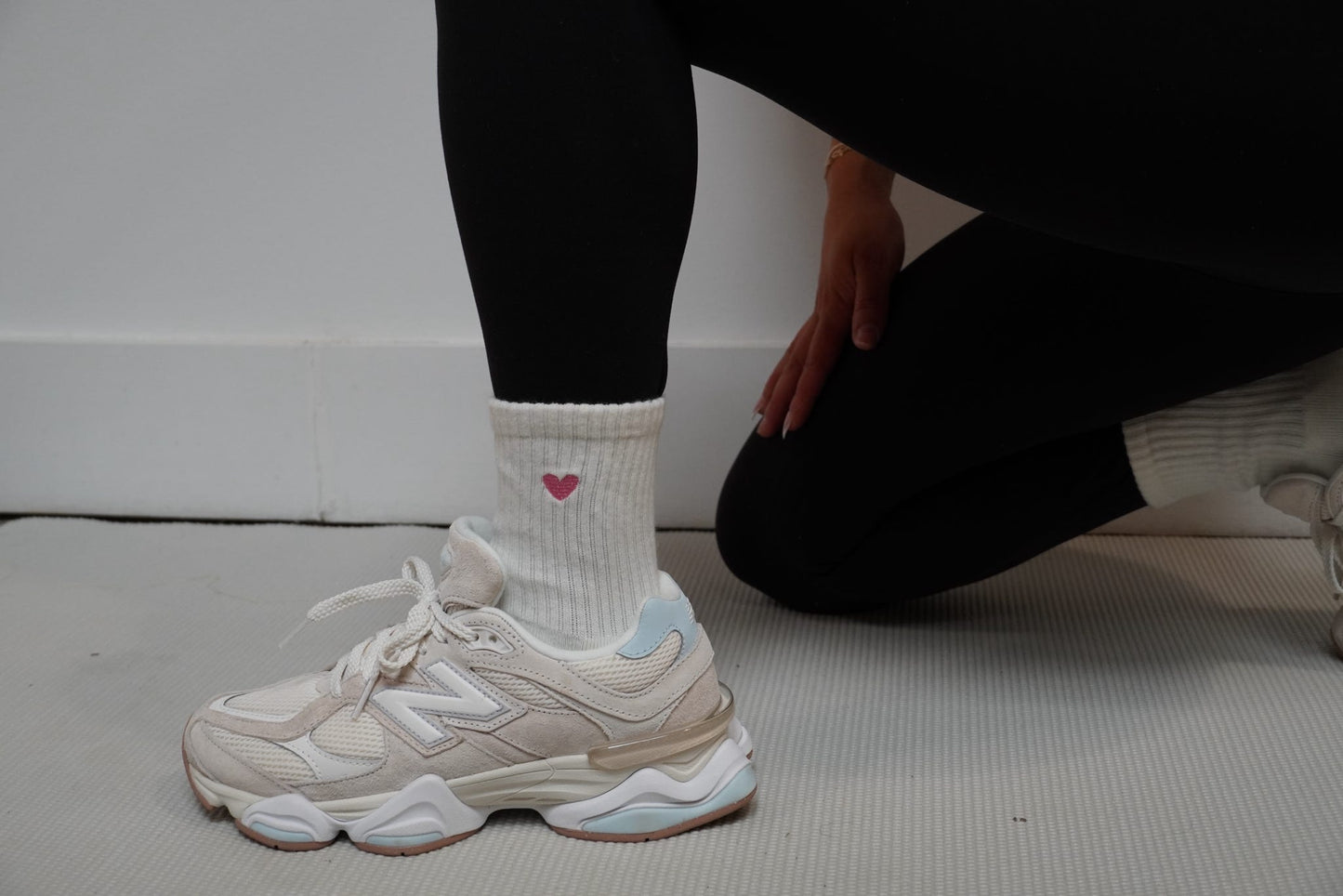 Person wearing white sneakers and a sock with a heart design on a light-colored floor.