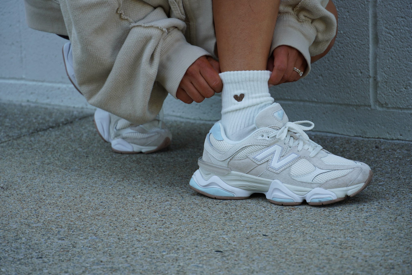 Person wearing white sneakers and a sock with a heart design sitting on concrete floor