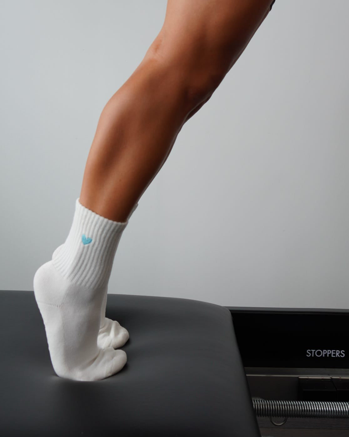 Person wearing white grip socks with an embroidered heart, standing on a black platform against a gray background.