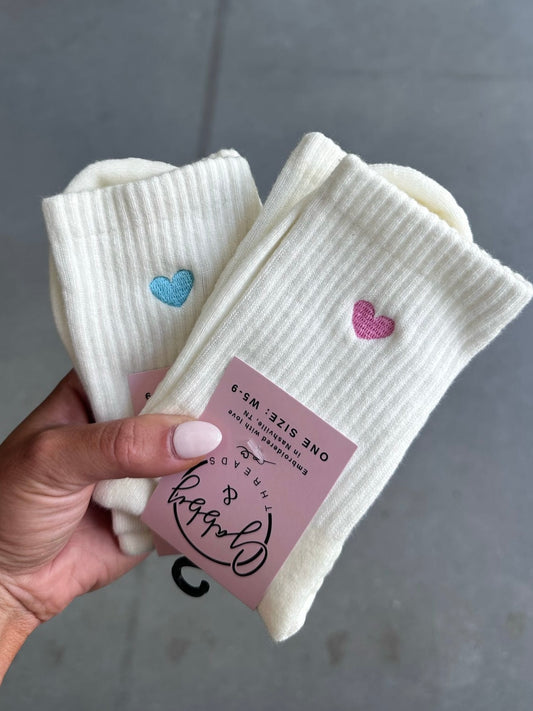 White socks with heart designs held by a hand against a gray background