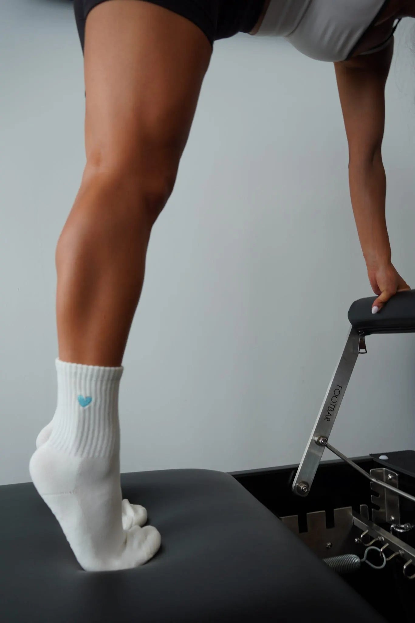 a person on a pilates reformer wearing white grip socks with an embroidered heart on them