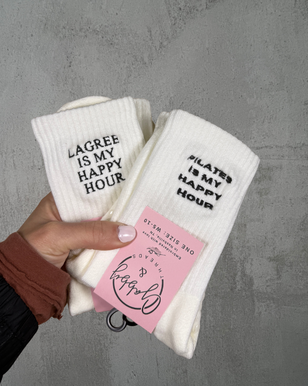 two pairs of white grip socks with the words "Lagree is my happy hour" and "pilates is my happy hour" embroidered on them