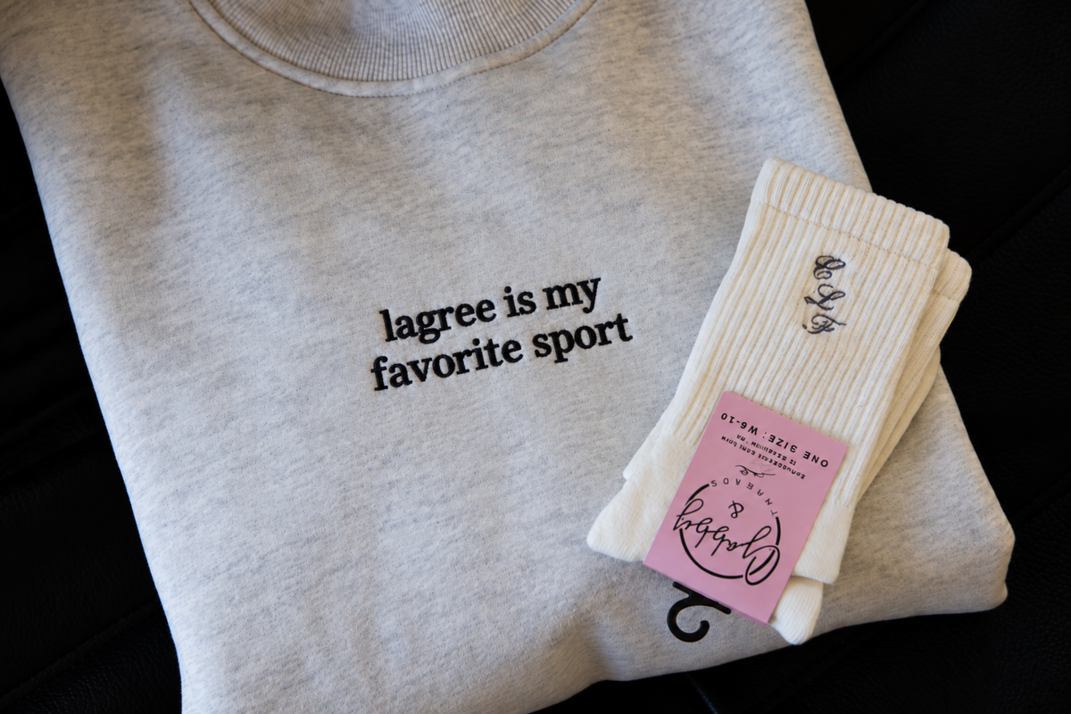 a folded mockneck sweatshirt featuringt the words "lagree is my favorite sport" with a pair of grip socks laying on top 