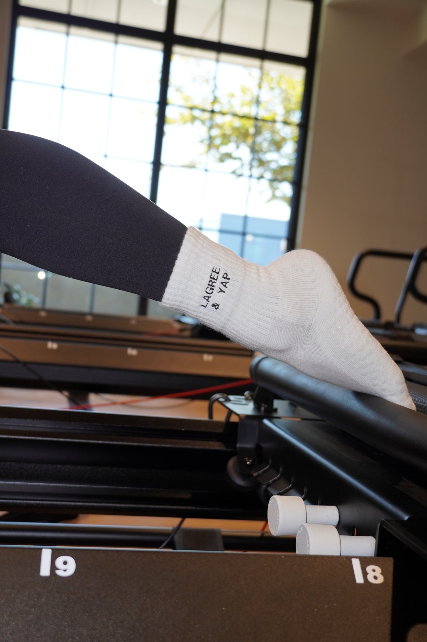 a person is on a reformer and wearing a pair of white grip socks that say "lagree & yap"