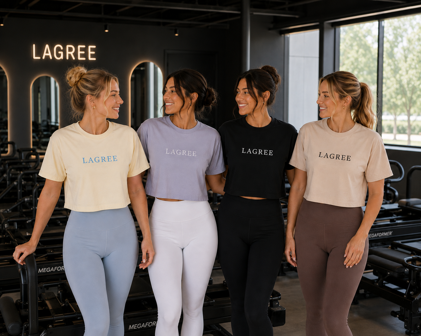 four woman are in lagree studio wearing a cropped  shirt that is embroidered with the word "LAGREE" embroidered on them