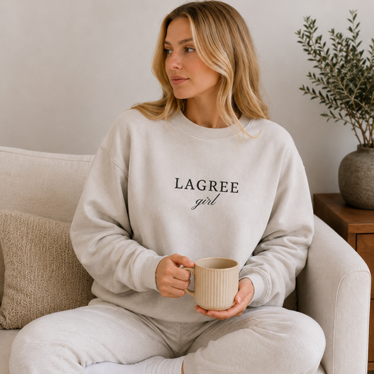 a girl is sitting on a couch wearing a lagree girl crewneck