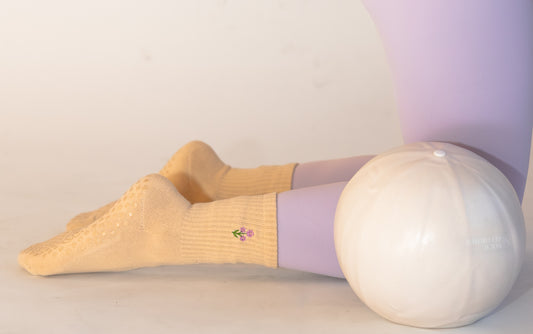a person is wearing a pair of beige socks with purple embroidered flowers on them. the person is wearing lilac colored leggings and is sitting next to a workout ball.