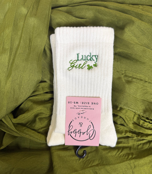 A pair of white pilates socks with the words "Lucky girl" embroidered on them with two clovers for St. Patrick's Day