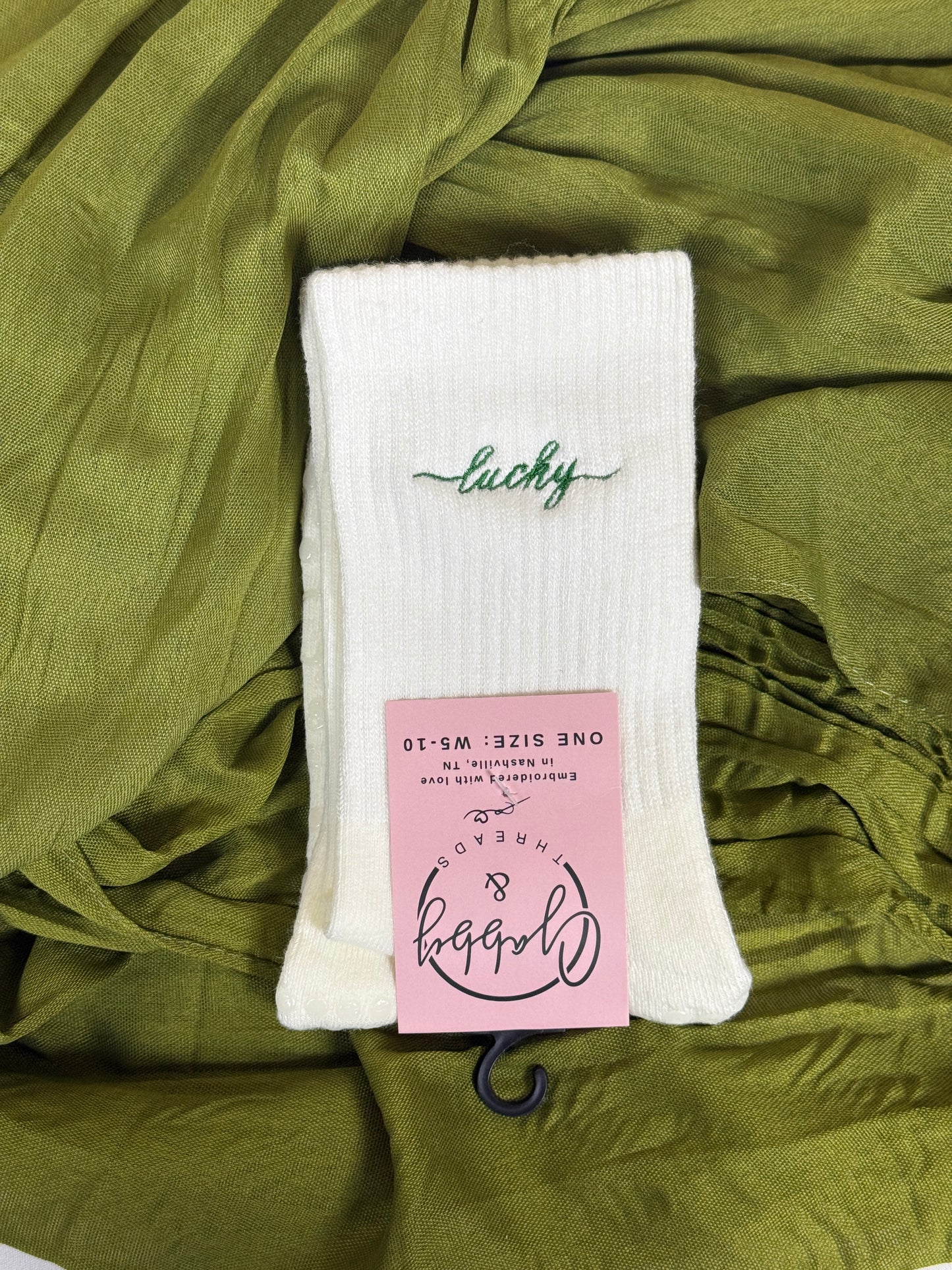 a pair of white grip socks for pilates with the word "lucky" embroidered in script font for St. Patricks Day