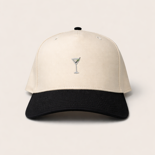 Two-tone cap with a martini glass emblem on a light beige background