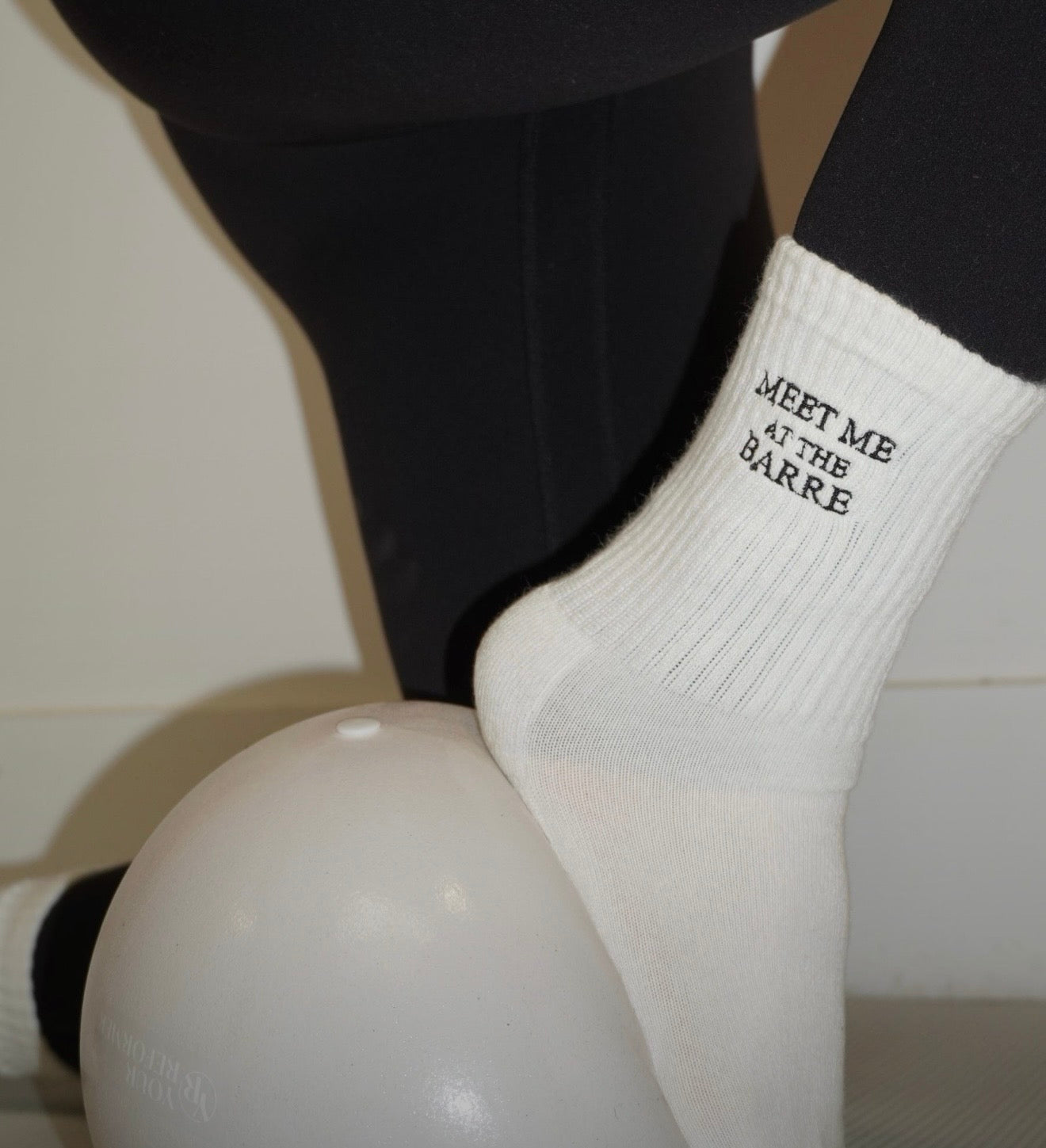 White sock with 'Meet Me at the Barre' text worn by a person who has their foot on a ball