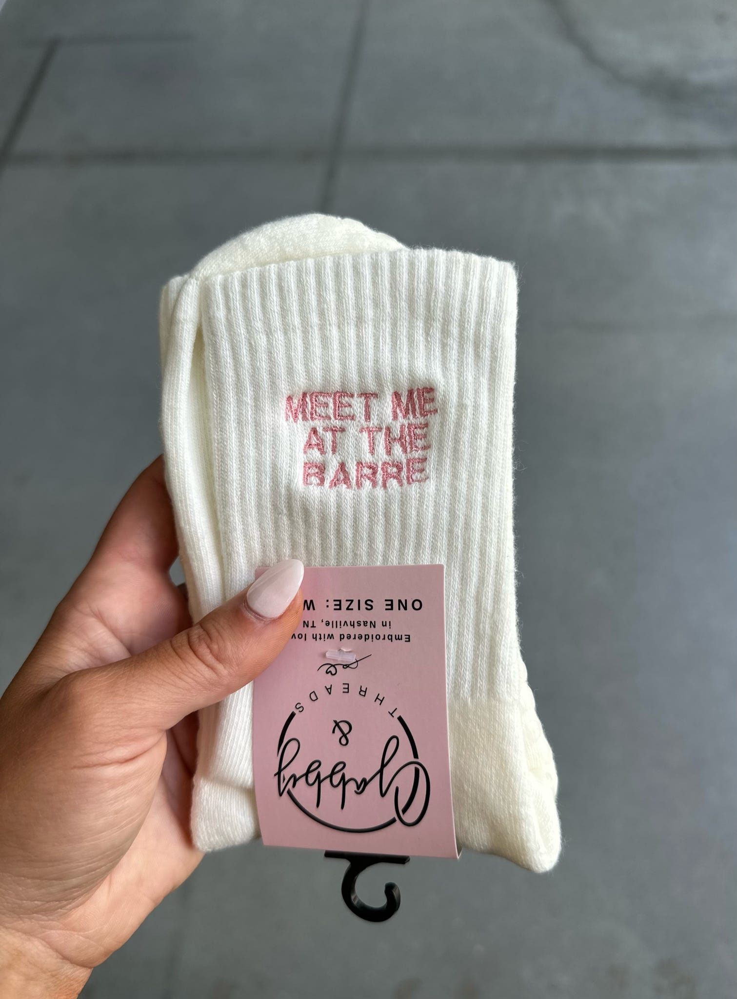 White sock with text held by a hand against a gray pavement background