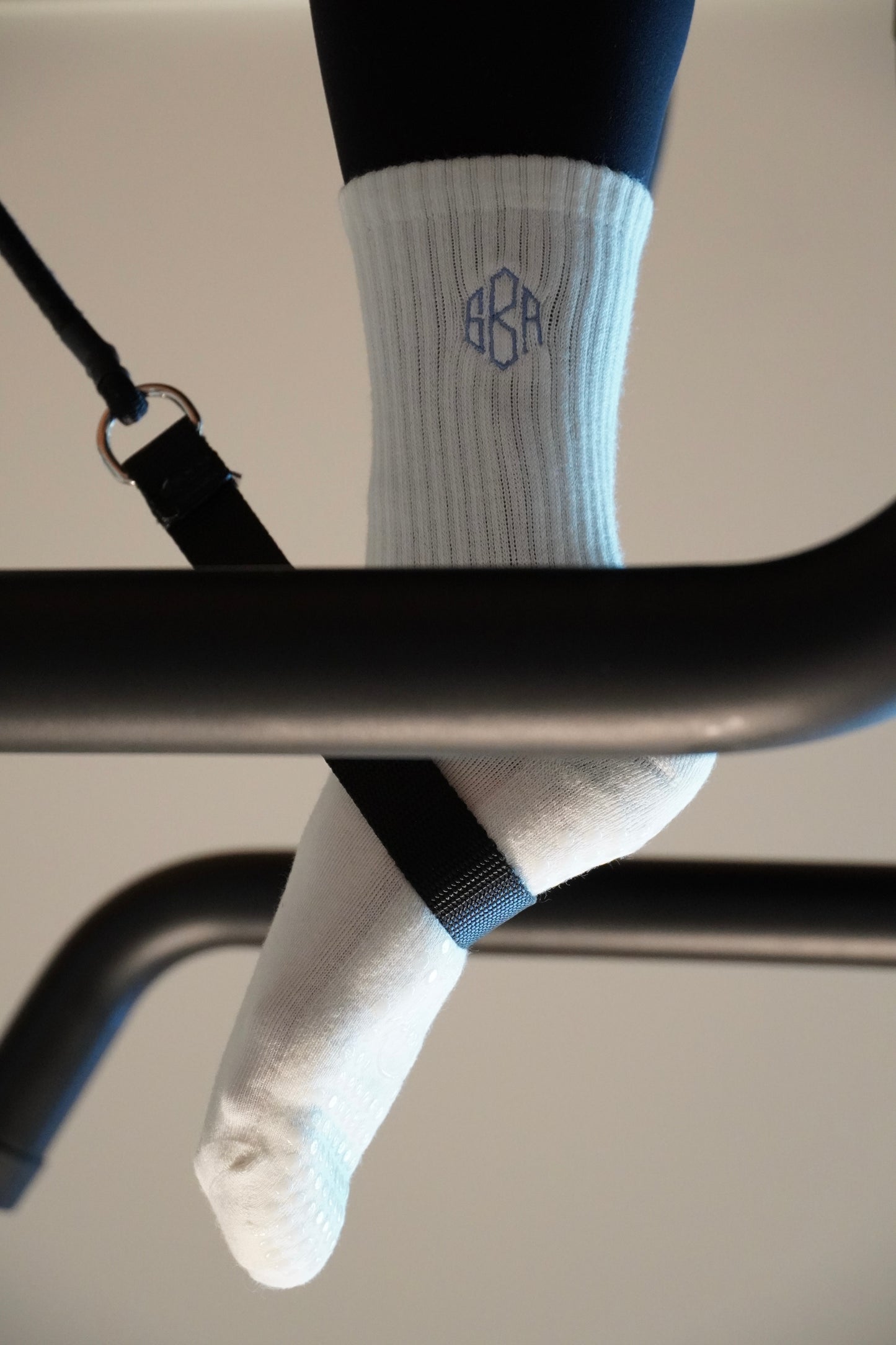 a person is wearing a pair of white grip socks that are embroidered with a custom monogram on a pilates reformer