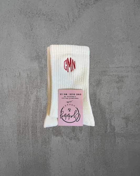 a pair of white grip socks with a three letter initial monogram embroidered on them