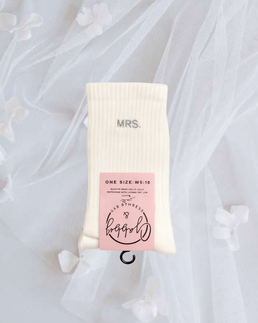 a pair of white embroidered grip socks with the text "Mrs." embroidered on it against a lace background