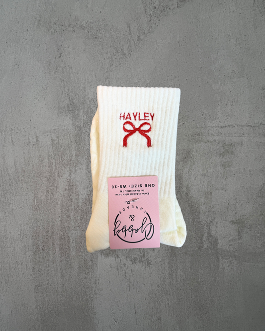 a pair of white grip socks with a bow and name embroidered on it