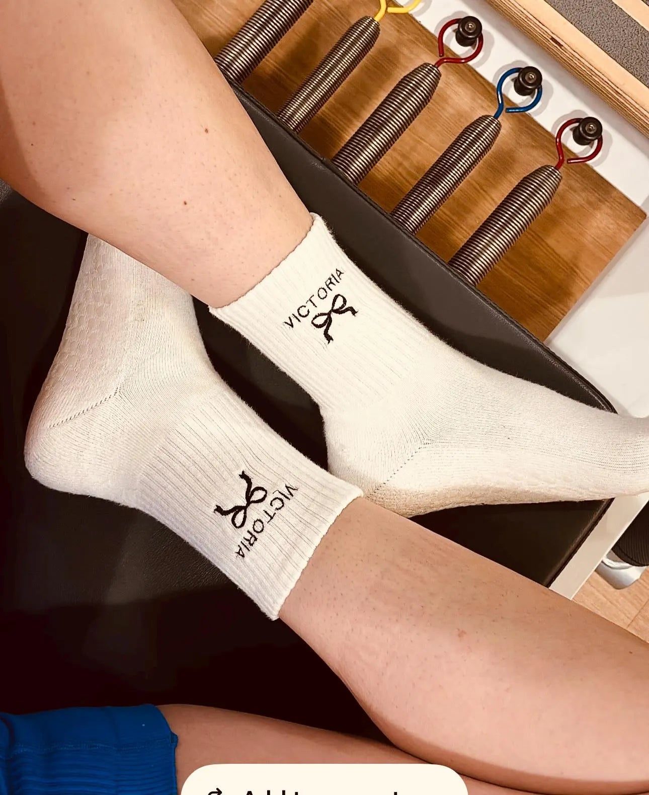 a person is sitting on a reformer with a pair of white grip socks on with their name embroidered on them
