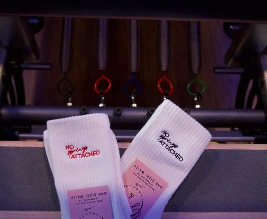 Two pairs of socks with text that says "no springs attached" on a pilates refromer