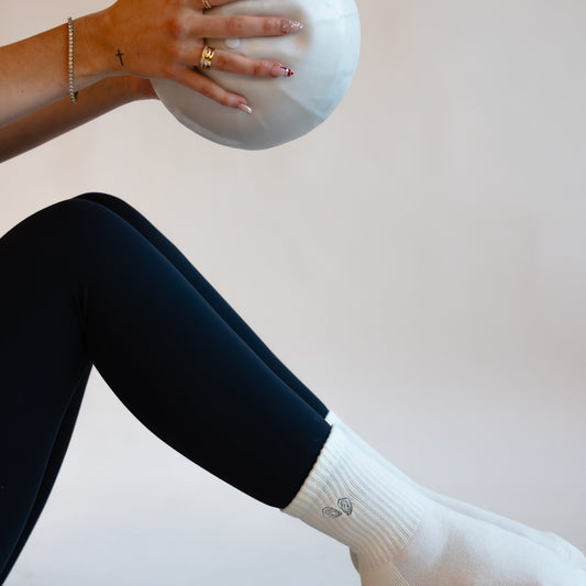 Person sitting on a yoga mat with a white ball under their legs against a plain background