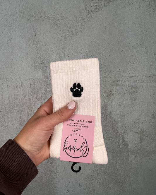 a pair of white grip socks with a paw print embroidered on it