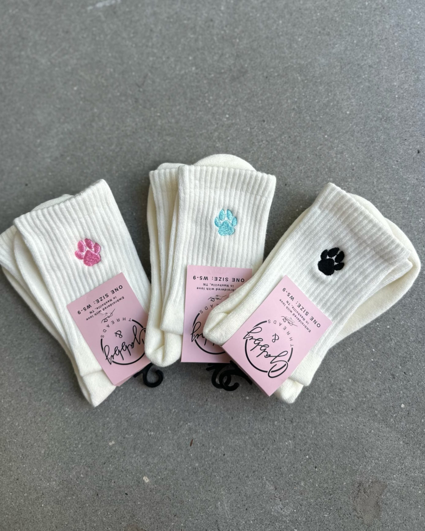 Three pairs of white socks with paw prints with pink labels on a gray surface