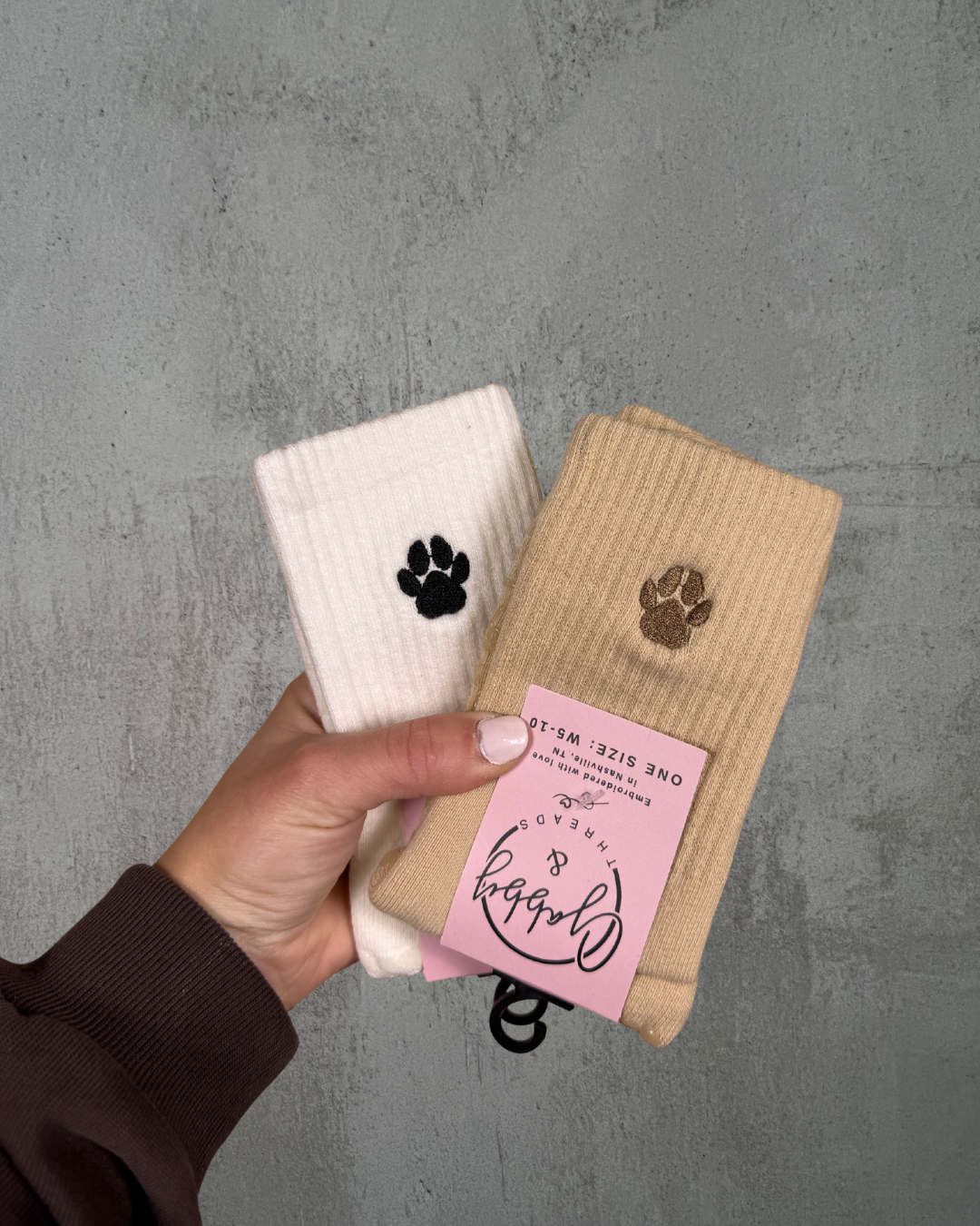 Two pairs of socks with paw prints held by a hand against a gray background