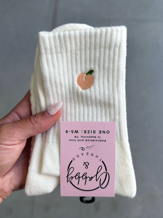 White sock with peach embroidery held by a hand, against a gray background